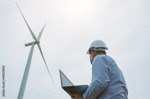 Engineers windmills wearing face mask and  working on laptop with the wind turbine in background