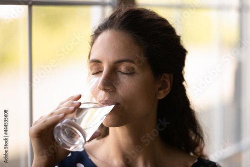 Calm woman drinking fresh pure water with closed eyes, satisfying thirst during heat weather, enjoying cold beverage, keeping healthy lifestyle, diet, hydration, metabolism. Healthcare concept