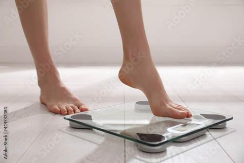Woman stepping on floor scales indoors, closeup. Weight control