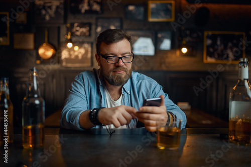 Man with mobile phone sitting at counter in bar