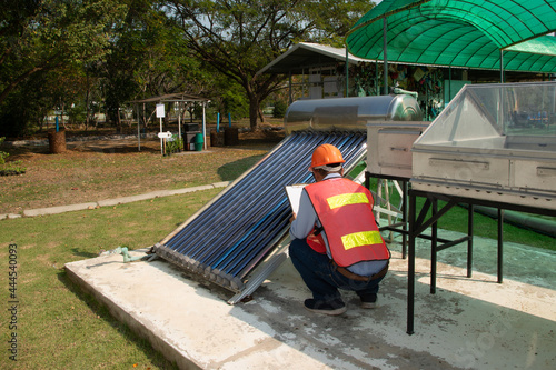 Foto The Asian worker in uniform and helmet checks concentrating Solar Power with Flat Plat collector and Evacuum Tube Collector