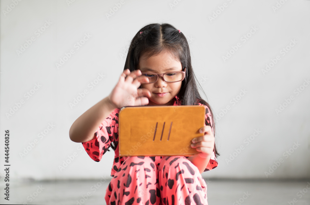 Asian child or kid girl smile wearing blue block glasses to learn from home or school study online on computer tablet and communication or people play game on smartphone and street to dirty white wall Asian child or kid girl smile wearing blue block glasses to learn from home or school study online on computer tablet and communication or people play game on smartphone and street to dirty white wall