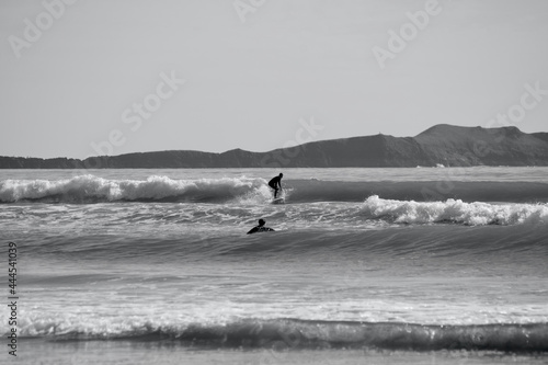 Silhouette images of surfers riding waves on Llangennith Beach on the Gower Peninsula. A popular sport for water sport activities with its sandy beach and rolling waves. Sun glistening on the water
 photo