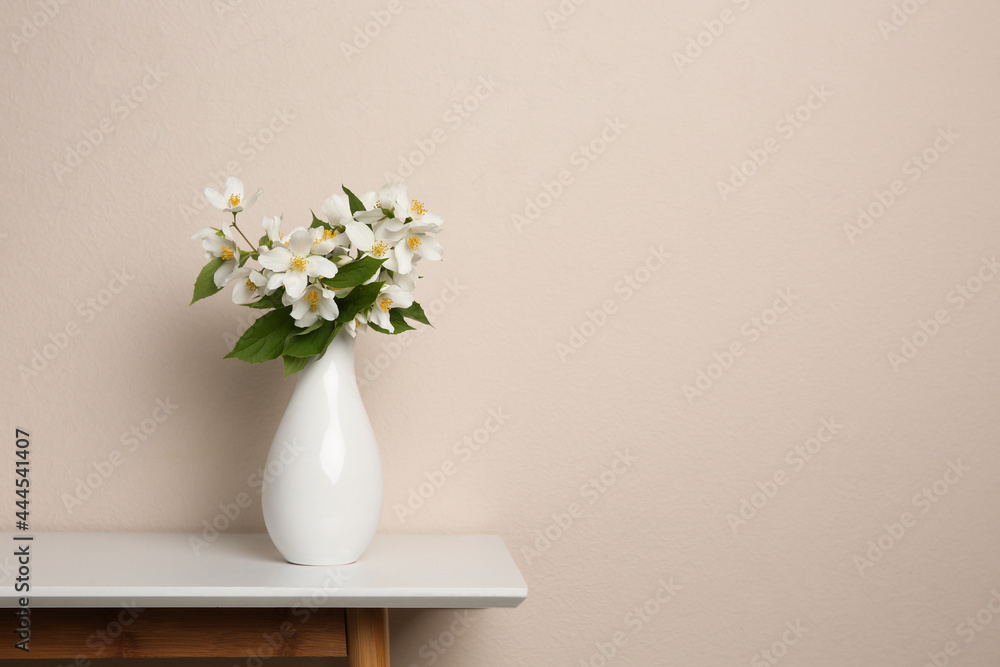 Bouquet of beautiful jasmine flowers in vase on table near beige wall, space for text