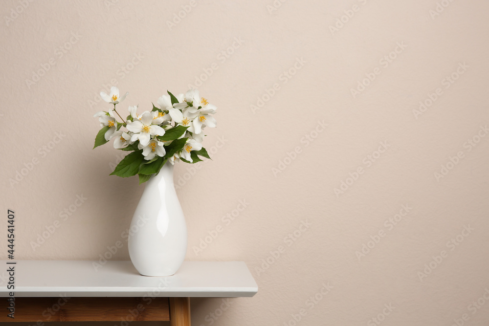 Fototapeta premium Bouquet of beautiful jasmine flowers in vase on table near beige wall, space for text