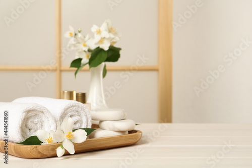Beautiful jasmine flowers, towels and spa stones on white wooden table, space for text