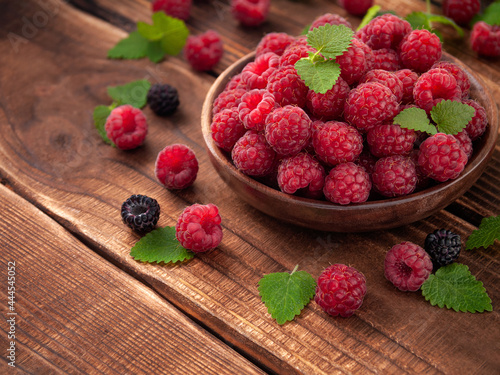 Ripe raspberries in a plate on wooden table in summer surrounded by berries and lemon balm leaves. Copy space, horizontal