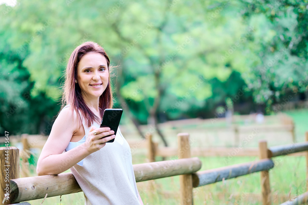 smiling young adult woman using smartphone in countryside smiling young adult woman using smartphone in countryside