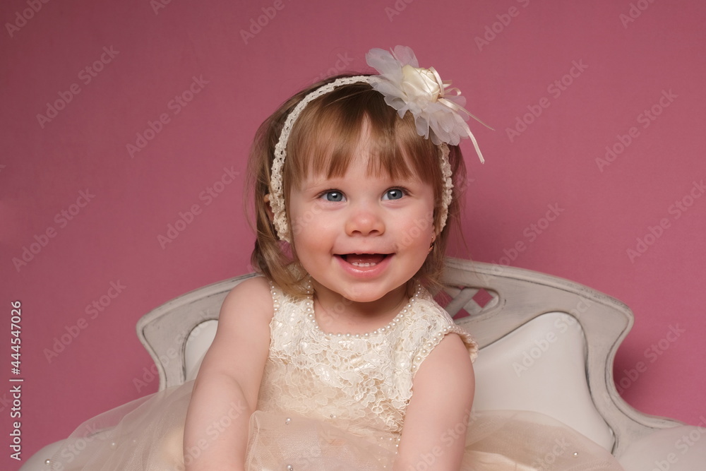 Children's studio photo session on a pink background A girl sits in a beige dress on a white sofa Children's studio photo session on a pink background A girl sits in a beige dress on a white sofa