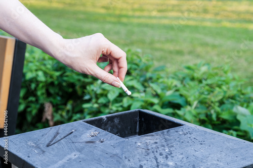 Fotografie Woman throws her cigarette butt into a metal trash can in a city park