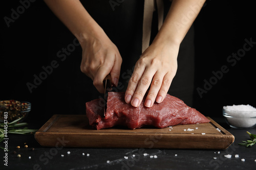 Fototapeta Naklejka Na Ścianę i Meble -  Woman cutting fresh raw meat at black table, closeup