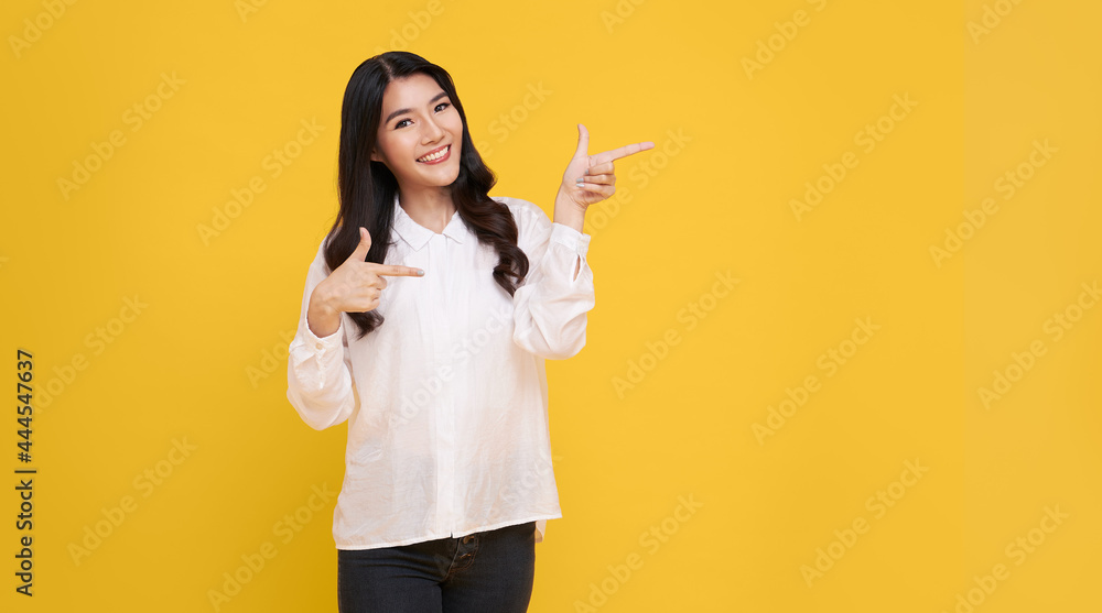 Happy young Asian woman standing with her finger pointing isolated over yellow banner background with copy space. Happy young Asian woman standing with her finger pointing isolated over yellow banner background with copy space.