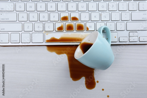 Cup of coffee spilled over computer keyboard on white wooden table, flat lay photo
