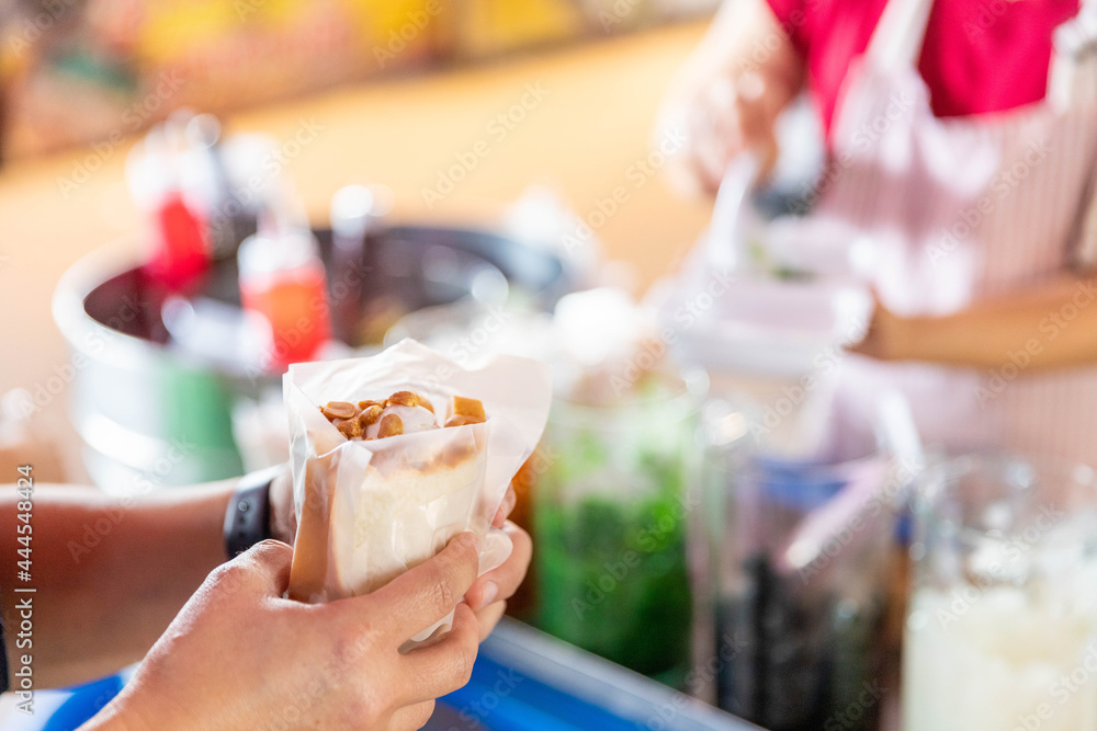 A vendor selling ice cream topped with nuts. to customers in the fresh market A vendor selling ice cream topped with nuts. to customers in the fresh market