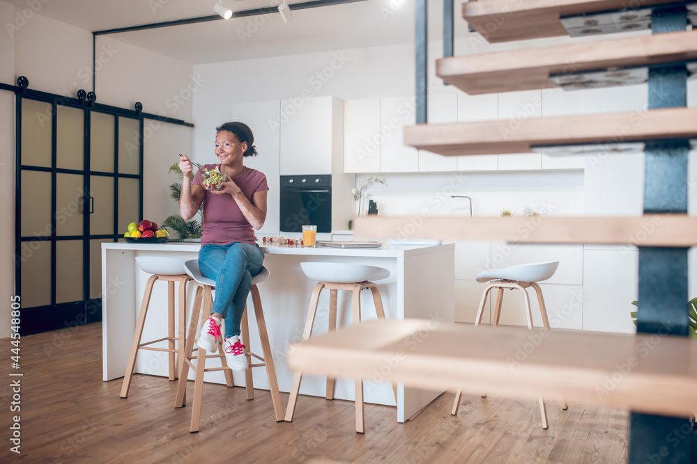 A dark-skinned woman sitting in the kitchen and eating salad A dark-skinned woman sitting in the kitchen and eating salad