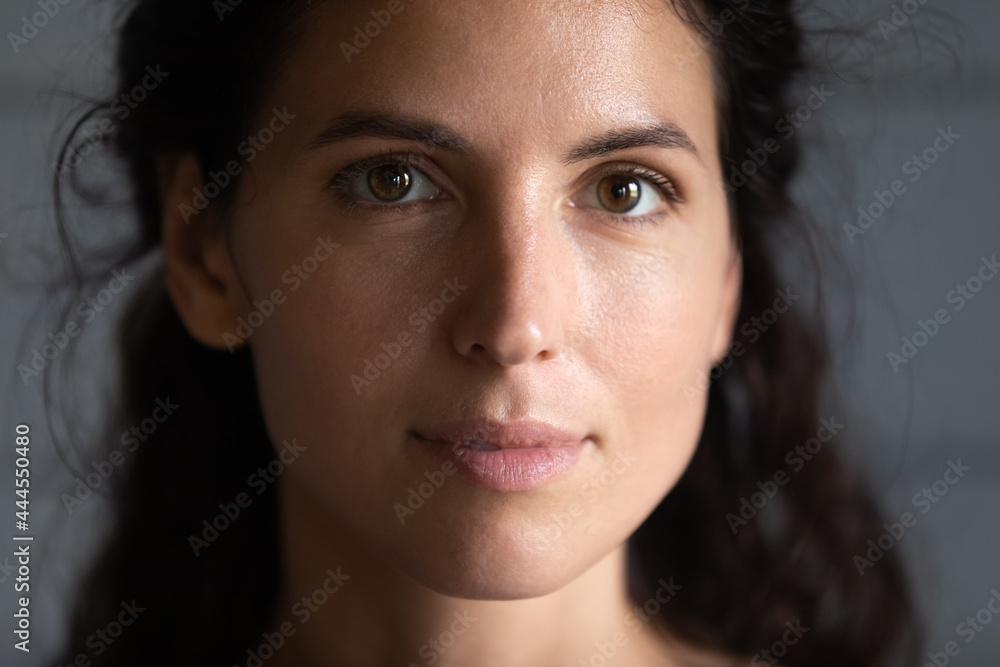 © fizkes - Close up portrait of serious beautiful millennial young woman with smooth healthy skin and black hair looking at camera. Face of Hispanic 30s female model on grey background. Beauty care concept