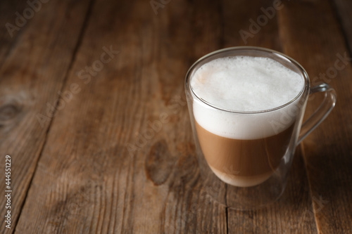 Hot coffee with milk in glass cup on wooden table. Space for text