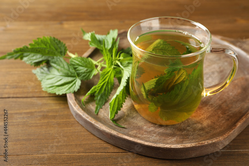 Glass cup of aromatic nettle tea and green leaves on wooden table