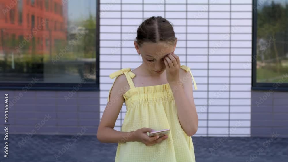 Teenager girl in yellow dress typing message in mobile phone outdoor. Young teen girl using smartphone on summer city street