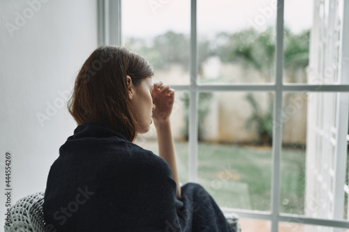 women at home covered herself with a blanket and looks out the window interior rest