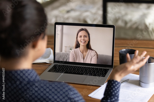 Happy young millennial colleagues having virtual talk, discussing work project. Teacher training student via video call. Women teaching and studying language online. Screen display view over shoulder
