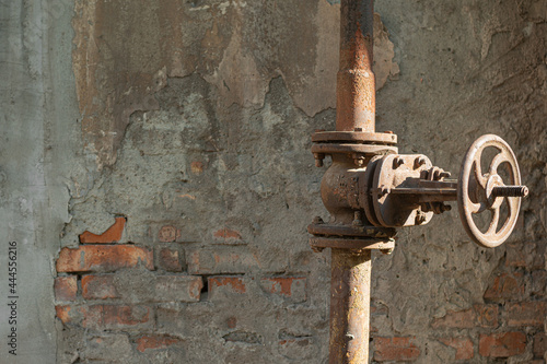 Old rusty pipe with valve on shabby brich wall background with free space for text  close-up.