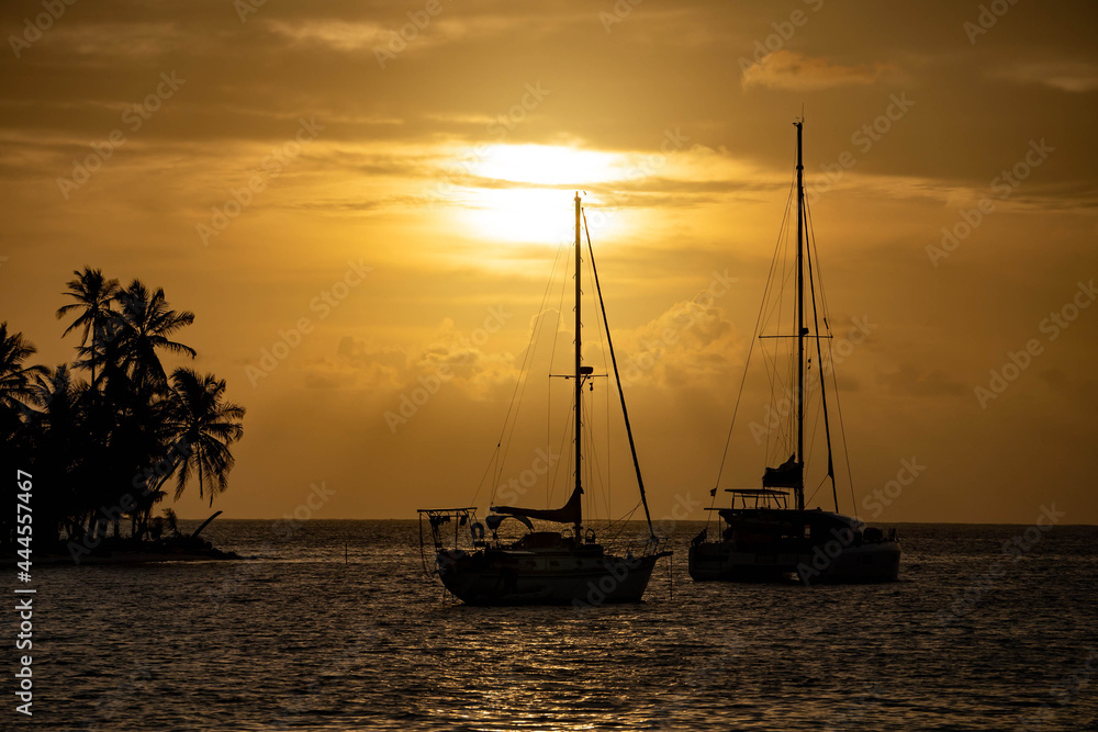 Beautiful sunset with silhouette of two sailboats and palm trees on island. Travel, freedom and adventure concept 