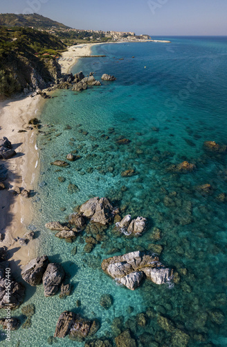 Aerial view of a beach and umbrellas. Tropea, Calabria, Italy. Parghelia. Overview of seabed seen from above, transparent water. Swimmers, bathers floating on the water. Beach and rocks of Vardanello