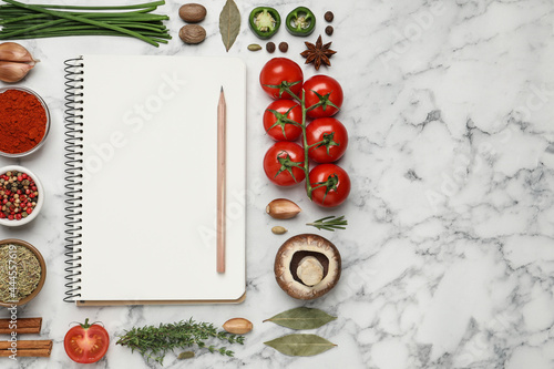 Open recipe book and different ingredients on white marble table, flat lay. Space for text