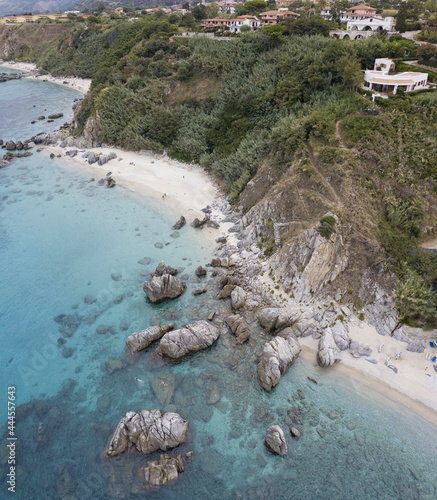 Aerial view of a beach and umbrellas. Tropea, Calabria, Italy.  Parghelia. Overview of seabed seen from above, transparent water. Swimmers, bathers floating on the water. Beach and rocks of Vardanello photo