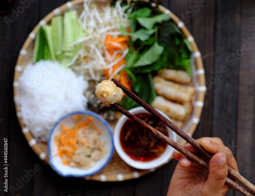 people hold chopsticks pick up fried spring rolls on tray of Vietnamese vegan food