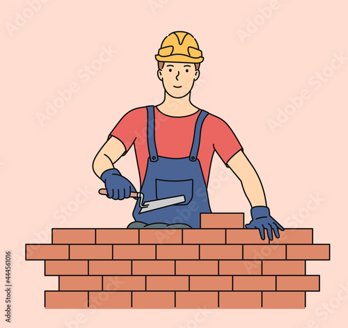Professional engineering and building. Young man bricks stacker in uniform with equipment makes wall.