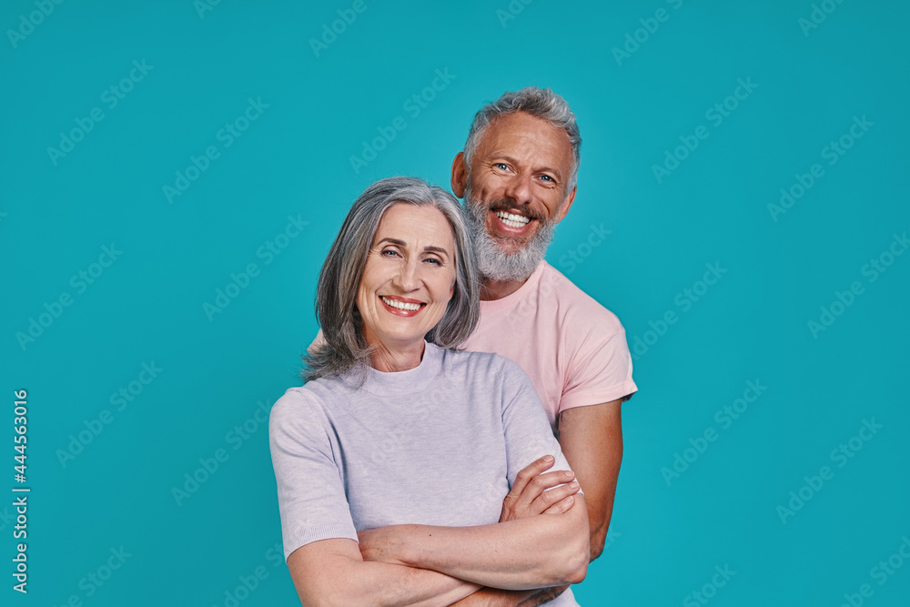 Beautiful senior couple looking at camera and smiling while standing together against blue background Beautiful senior couple looking at camera and smiling while standing together against blue background