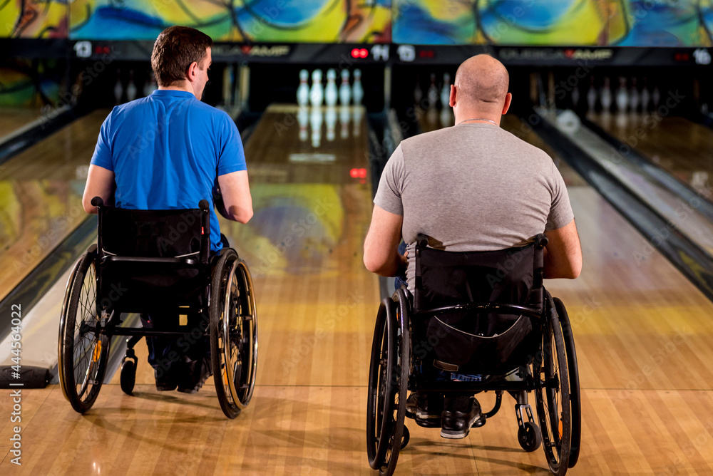 Obraz premium Two young disabled men in wheelchairs playing bowling in the club