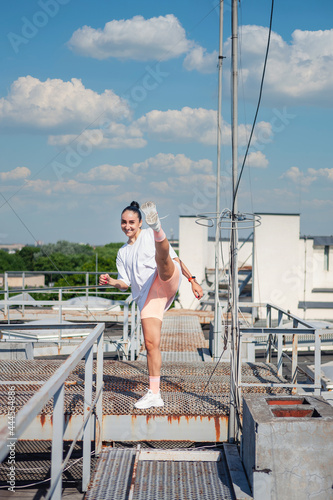 Young woman in a  sport dress is dancing on the roof of a building against the background of the cityscape and the summer sky