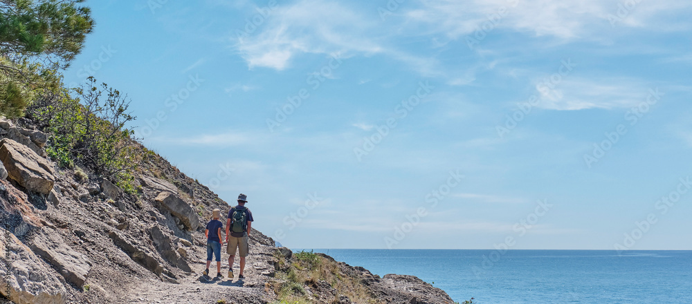 Boy and man hiking on the scenic Golitsyn trail. National botanical reserve New World, Crimea. View from back