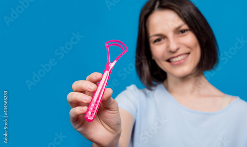 Bilde på lerret Beautiful happy young woman with tongue scraper on blank blue background