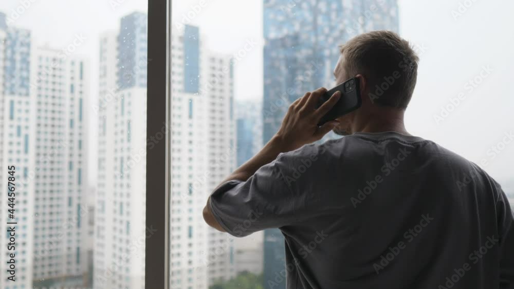 Back view of a man calling someone while looking out the window at the skyscrapers Back view of a man calling someone while looking out the window at the skyscrapers