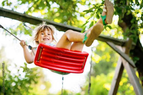 Happy little toddler girl having fun on swing in domestic garden. Smiling positive healthy child swinging on sunny day. Preschool girl laughing and crying. Active leisure and activity outdoors.
