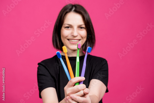 Beautiful happy young woman with different colored toothbrushes on blank pink background