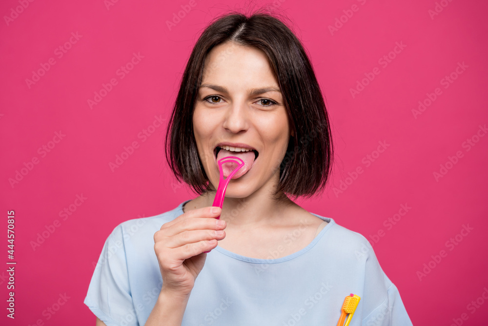Beautiful happy young woman with tongue scraper on blank pink background Beautiful happy young woman with tongue scraper on blank pink background