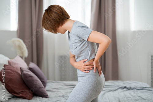 Back pain, kidney inflammation, woman suffering from backache at home photo