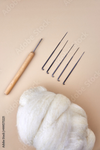 Needles and skein of wool for felting on a beige background.