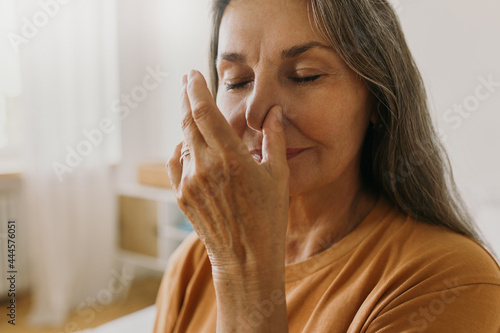Middle-aged woman practicing yoga breathing technics at home. Elderly female breathing with one nostril. Surya bheda pranayama concept. Meditation idea photo