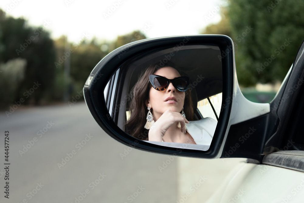 Young adult latin girl sitting inside the car looking in the rear view mirror
