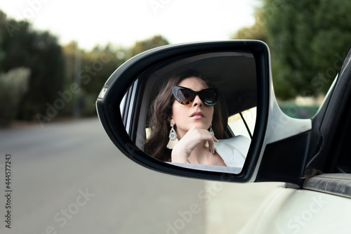 Young adult latin girl sitting inside the car looking in the rear view mirror