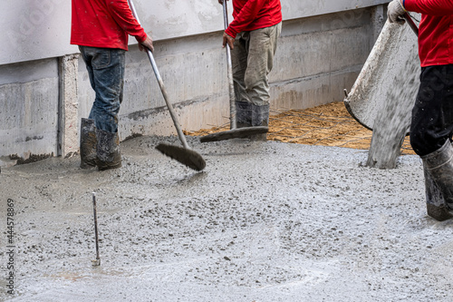 three worker team working wet cement on floor by use trowel with long Tools spreading poured concrete on golden sand for strong street after dry.