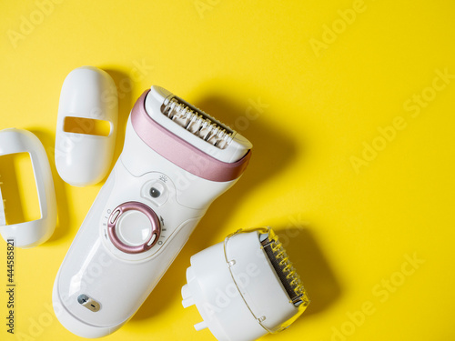 Female electric epilator in white on a yellow background. There are additional attachments nearby. Top view, flat lay photo