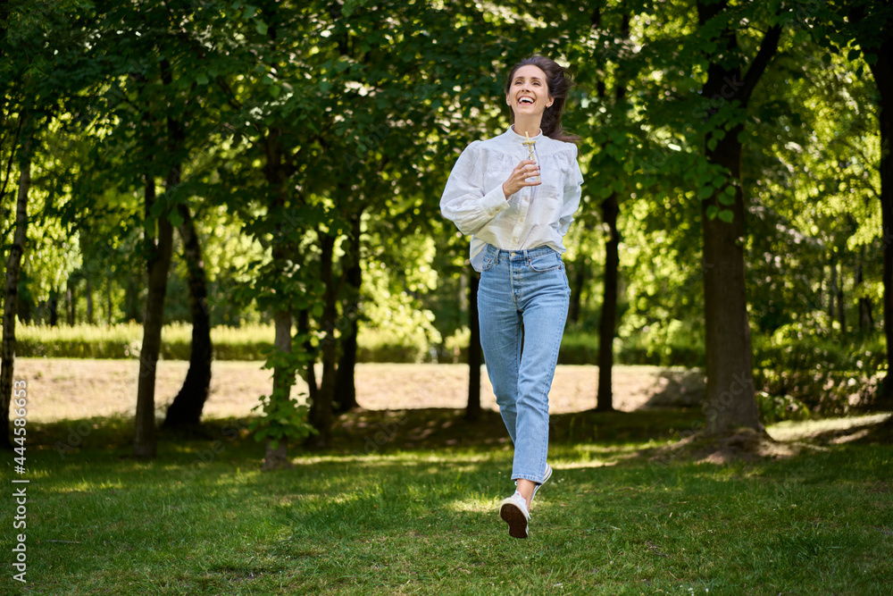 Joyful young woman running on the grass in the park wearing casual clothes Joyful young woman running on the grass in the park wearing casual clothes