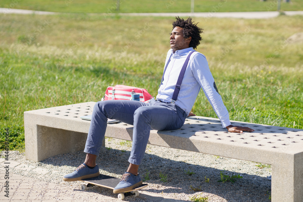 Black man with afro hair taking a coffee break sitting on a park bench.